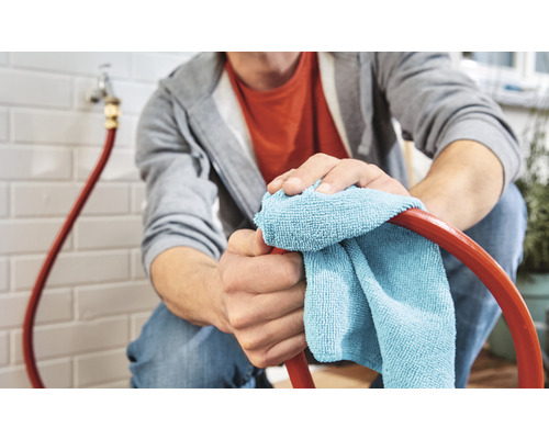 Mann reinigt einen Gartenschlauch mit einem Tuch.