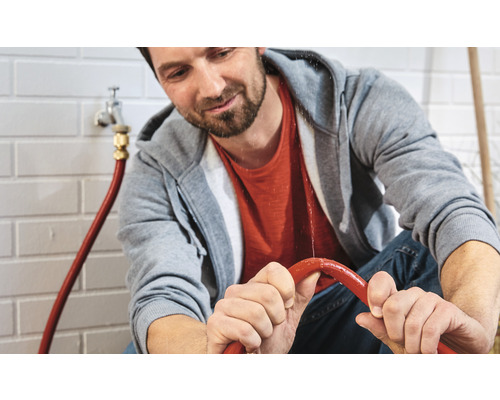 Mann hält einen undichten Wasserschlauch