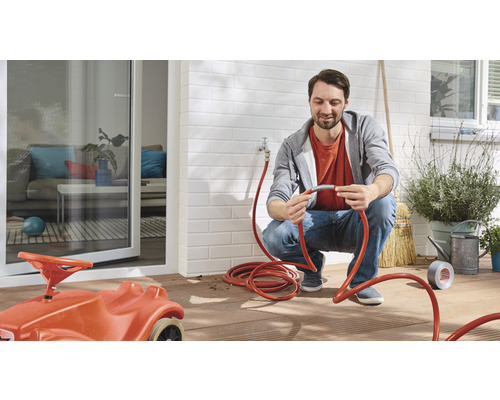 Mann verbindet Gartenschlauch auf Terrasse mit Kinderspielzeugauto.
