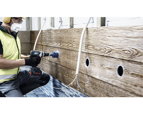 Ein Handwerker bohrt ein Loch in eine Holzwand mit einer Bohrmaschine für Elektroinstallationen.