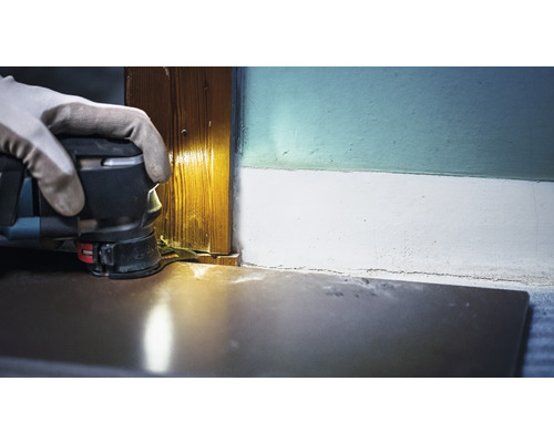 Une personne utilise une ponceuse multifonction pour poncer un montant de porte en bois.