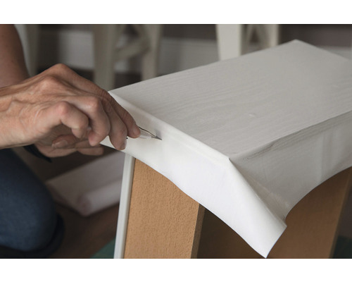 Une personne découpe du film sur un meuble avec un couteau de bricolage.