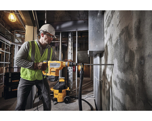Un homme perce un trou dans un mur en béton avec un marteau perforateur de la marque DeWalt.