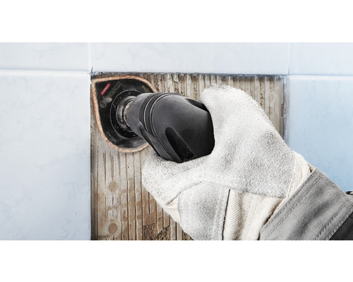 Main avec gant de protection enlevant des carreaux avec un outil multifonction