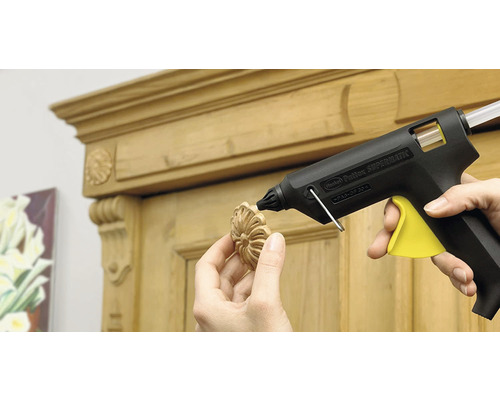 Heissklebepistole beim Anbringen eines Holzornaments an einem Schrank