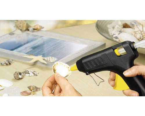 Heissklebepistole beim Anbringen einer Muschel auf einem Bilderrahmen