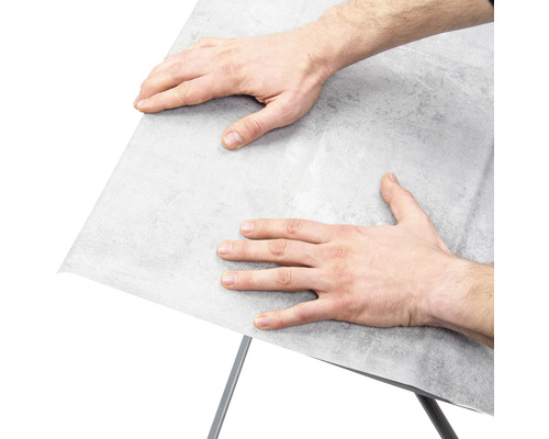 Un homme fixe un film pour meubles sur une surface.