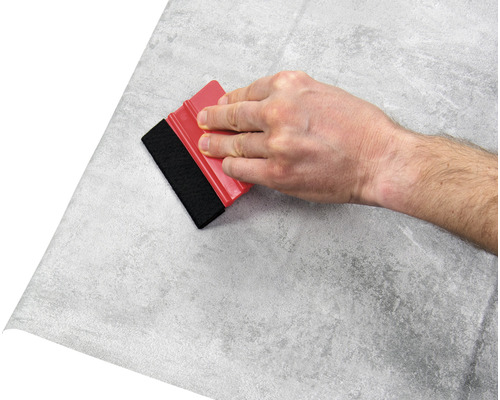 Main avec raclette appliquant un film à motif de pierre