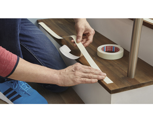 Person klebt Tesa-Kreppband auf eine Holztreppe