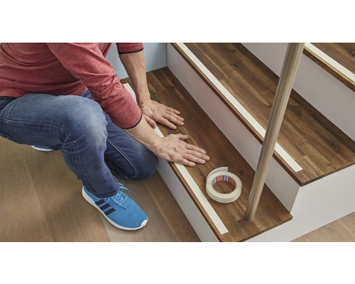 Mann befestigt Antirutschband auf einer Holztreppe.