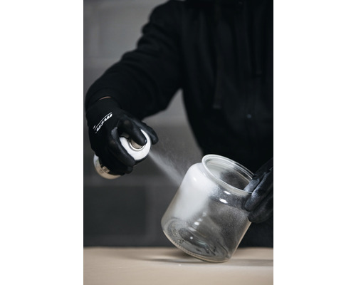 Eine Person sprüht Farbe aus einer Sprühdose in ein offenes Glasgefäß.