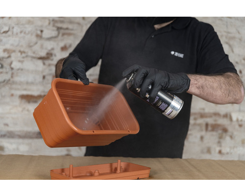 Une personne vaporise une jardinière avec de la peinture en aérosol.