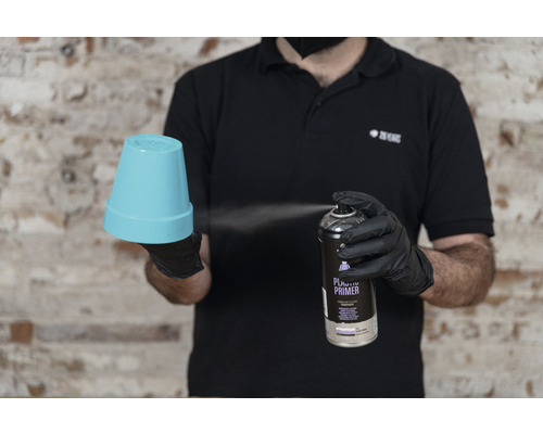 Une personne vaporise un pot de fleurs avec un apprêt plastique.