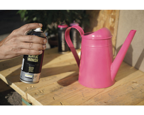 Une personne tient une bombe de vernis acrylique à côté d''un arrosoir sur une palette en bois.