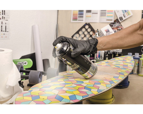 Une personne porte des gants et vaporise du vernis acrylique sur une planche à roulettes.