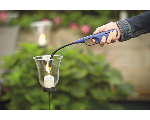 Eine Person zündet mit einem Stabfeuerzeug eine Kerze in einem Glas an.