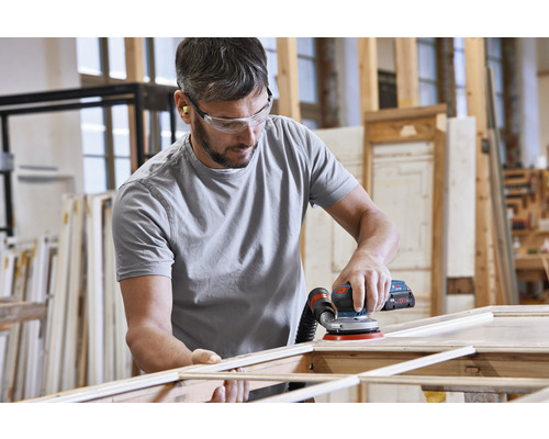 Un homme ponce du bois avec une ponceuse excentrique dans un atelier.