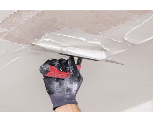Une main avec une spatule applique du mastic au plafond.