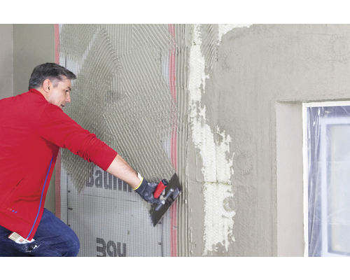 Un homme applique de l''enduit sur un mur avec le logo Baumit.