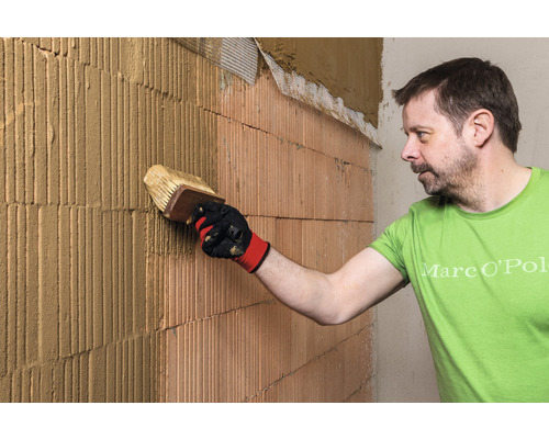 Un homme applique du plâtre sur un mur en briques