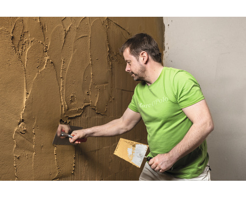 Mann trägt Putz mit einer Maurerkelle auf eine Wand auf.