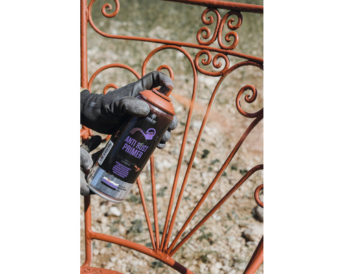 Une personne vaporise un apprêt antirouille sur une balustrade en métal.