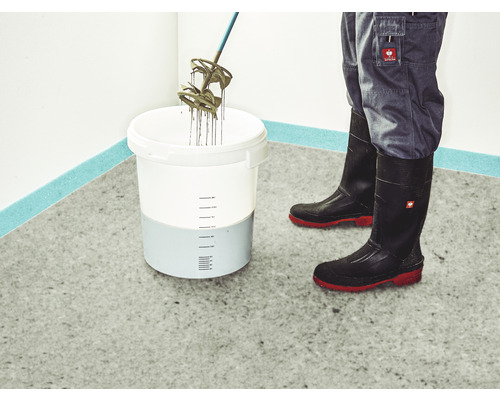 Le mortier est mélangé dans un seau avec un mélangeur, des bottes en caoutchouc et un pantalon de travail sont portés.