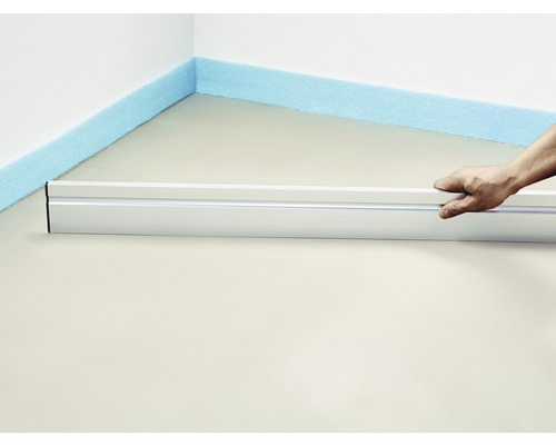 Une personne nivelle une chape avec une règle et des bandes d''isolation sur le mur