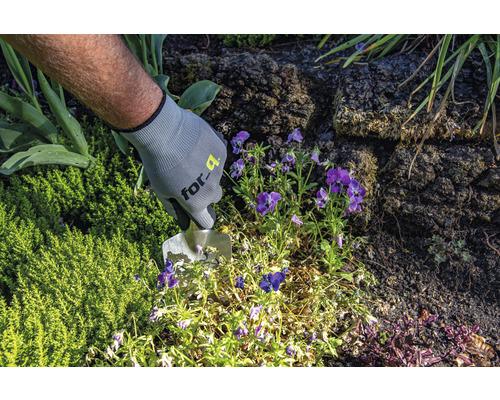 Eine Person mit Gartenhandschuhen arbeitet mit einer Pflanzkelle im Gartenbeet.