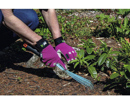 Eine Person harkt mit einem Rechen Gartenabfälle, geschützt durch Gartenhandschuhe.