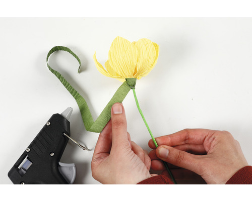 Personne fabriquant une fleur en papier avec un pistolet à colle chaude