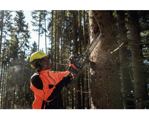 Un homme portant un équipement de protection coupe un arbre avec une tronçonneuse Metabo.