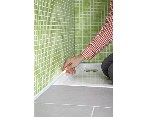 Jointoiement d''un receveur de douche avec du silicone dans une salle de bains carrelée en vert.