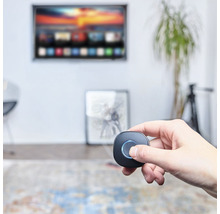 Une main tient une commande domotique devant un téléviseur