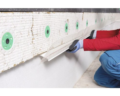 Une personne fixe un profilé de finition d''enduit sur un mur avec isolation thermique.