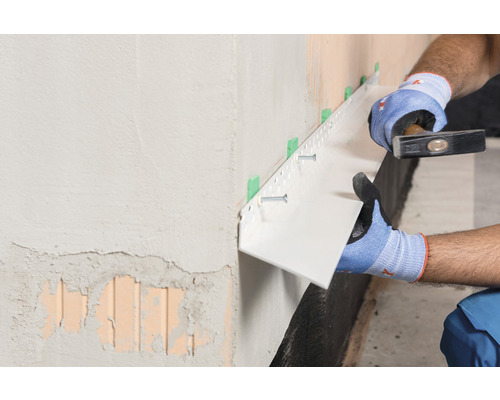 Artisan fixant un profilé de protection de socle au mur avec un marteau et des vis.
