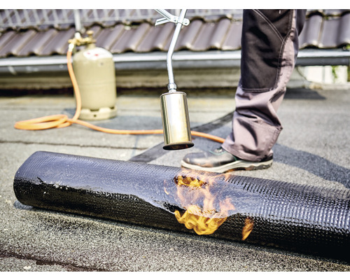 Couvreur soudant une membrane bitumineuse avec un chalumeau, bouteille de gaz à l''arrière-plan