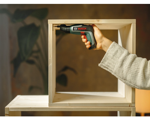 Une personne assemble une étagère en bois avec un tournevis sans fil de la marque Bosch.