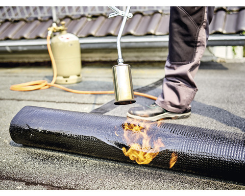 Couvreur soude une membrane de toit sur un toit avec un brûleur à gaz.