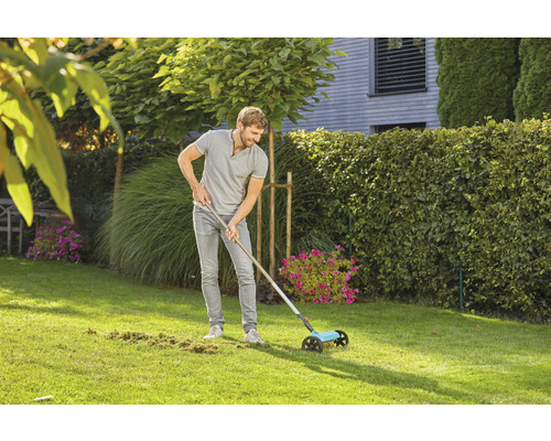 Un homme utilise un ramasse-gazon dans le jardin pour enlever les déchets de gazon.