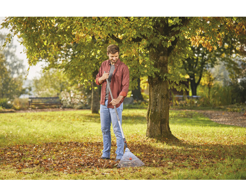 Mann mit Laubbesen im Garten, Herbstlaub auf dem Rasen.