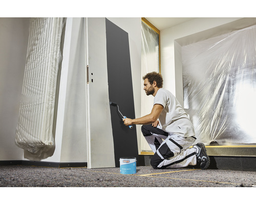 Un homme peint une porte avec un rouleau à peinture et de la peinture