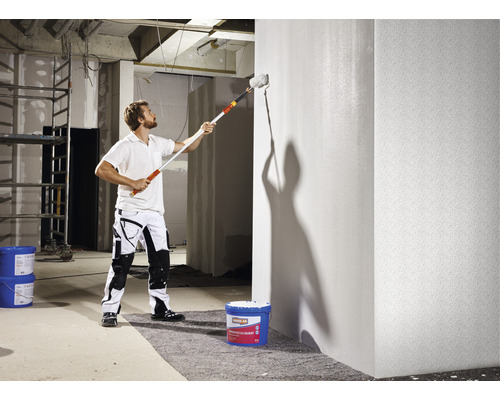Un homme peint un mur avec un rouleau à peinture dans un chantier.