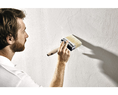 Un homme peint un mur avec une brosse plate.