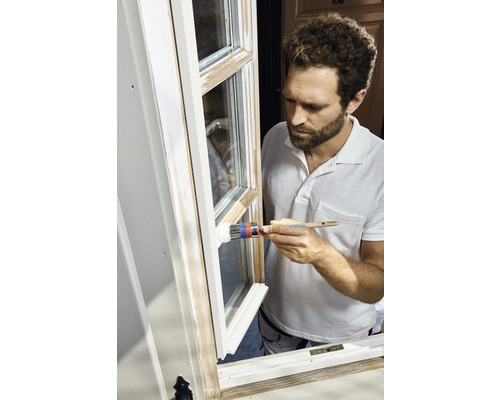 Mann streicht Fensterrahmen mit Pinsel und Farbe.