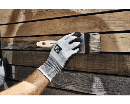 Une personne porte des gants et peint du bois avec un pinceau.