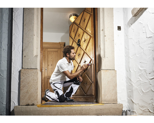 Handwerker streicht eine Holztür mit Sternmuster und Ornamenten mit einem Pinsel.