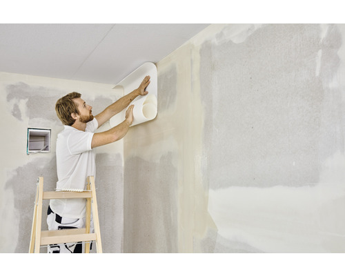 Un homme tapisse un mur avec un rouleau de papier peint sur une échelle