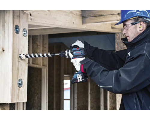 Un artisan perce un trou dans une poutre en bois avec une perceuse-visseuse sans fil.
