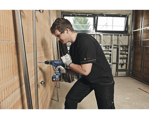 Un homme perce un trou dans un mur sur un chantier avec une perceuse.